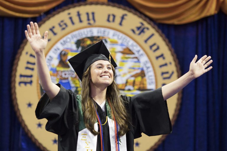 Student smiling with arms raised at their graduation.